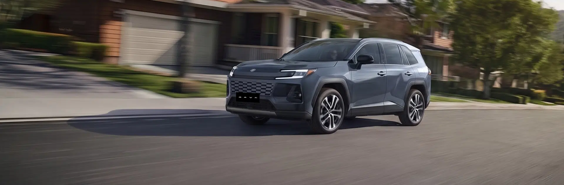 Gray SUV cruising down a residential street with houses and trees, motion blur suggesting speed in daytime.