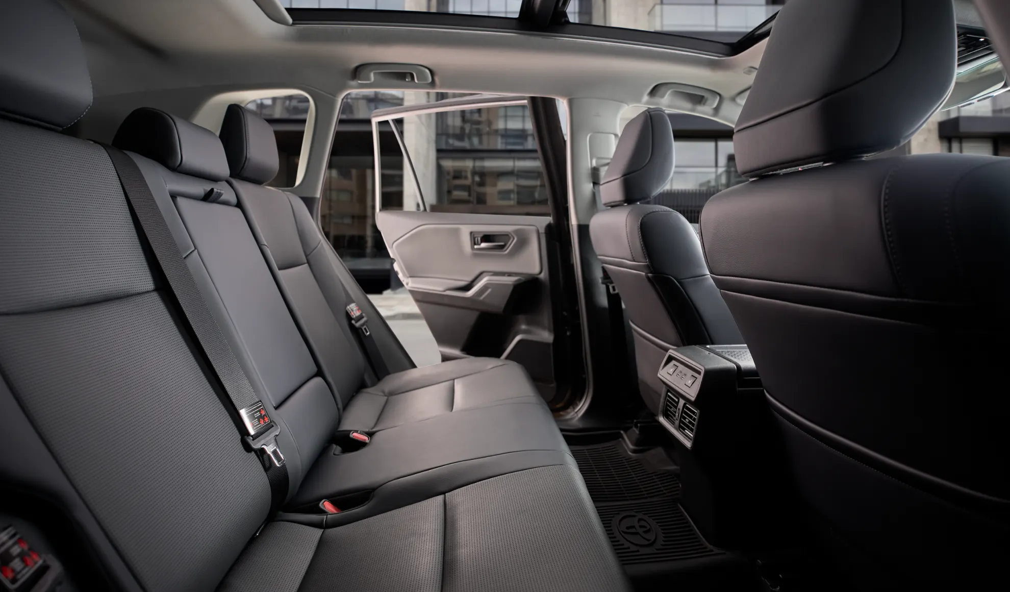 Rear seats in a dark leather SUV interior with an open rear door and panoramic sunroof visible in the background, conveying spaciousness and comfort.