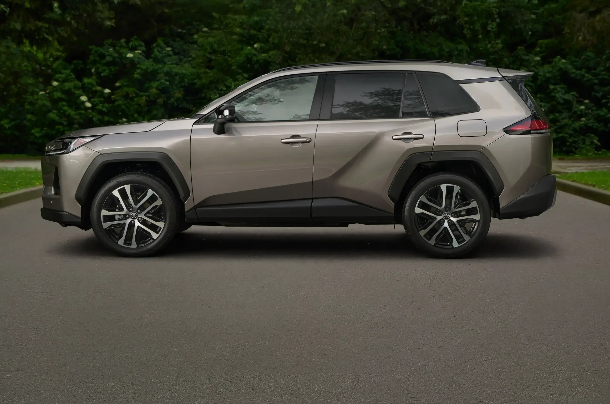 Side view of a silver SUV parked on a paved lot with a green hedge in the background.
