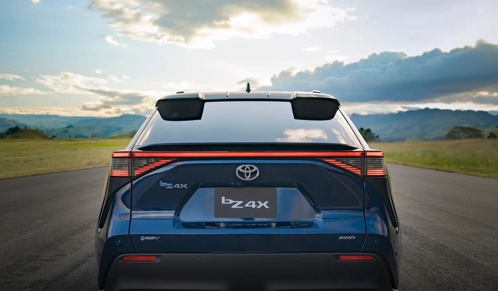Rear view of a black Toyota bZ4X SUV on a road with mountains in the distance; taillights lit and hatch visible.