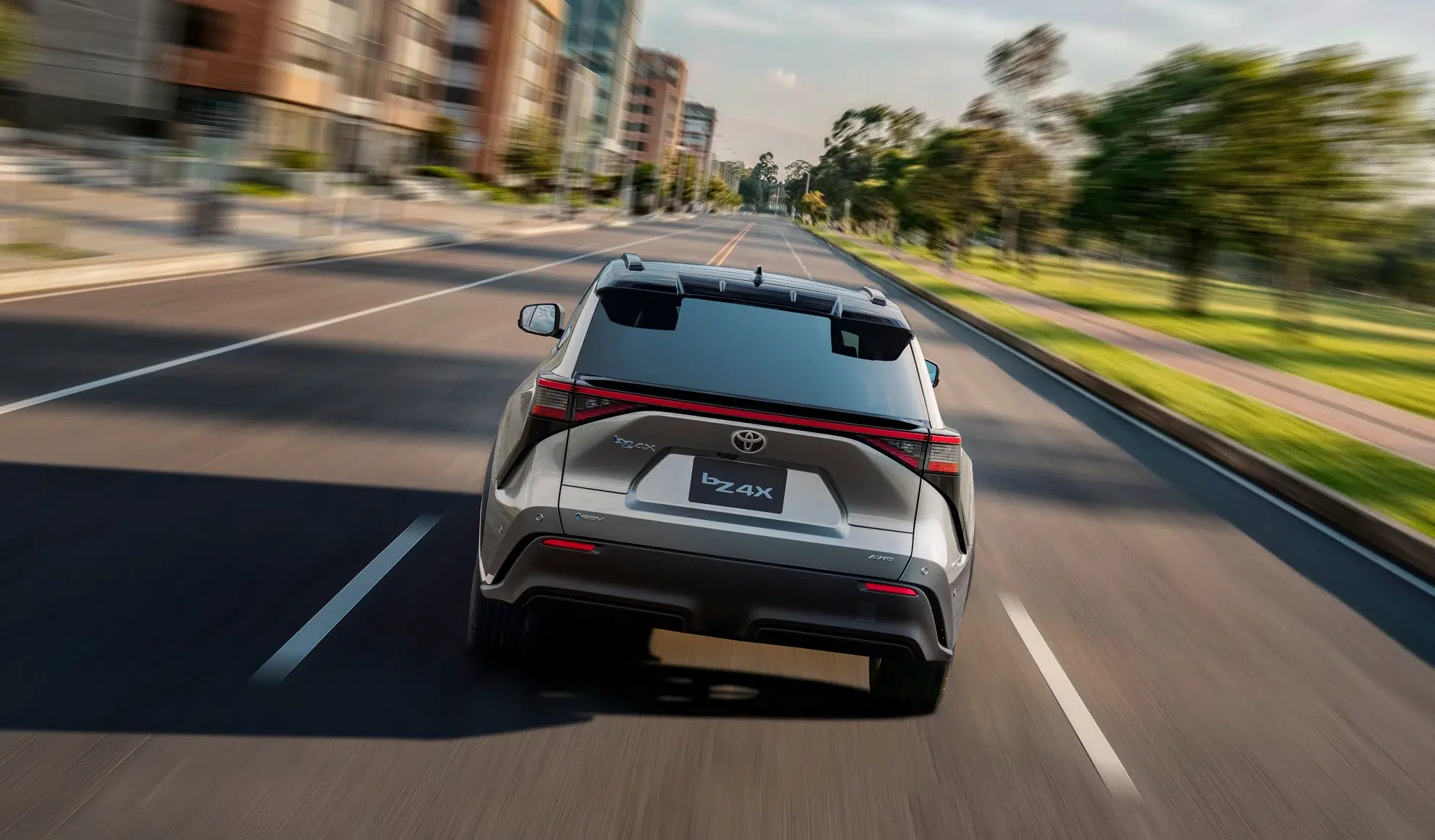 Rear view of a white Toyota bZ4X SUV driving away on a city street with motion blur in the background