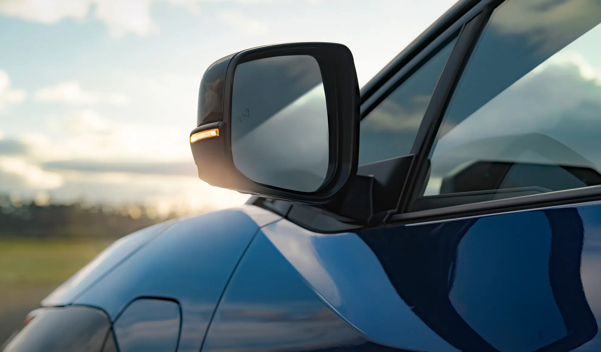 Close-up of a blue car's side-view mirror with the turn signal lit and a blurred landscape in the background