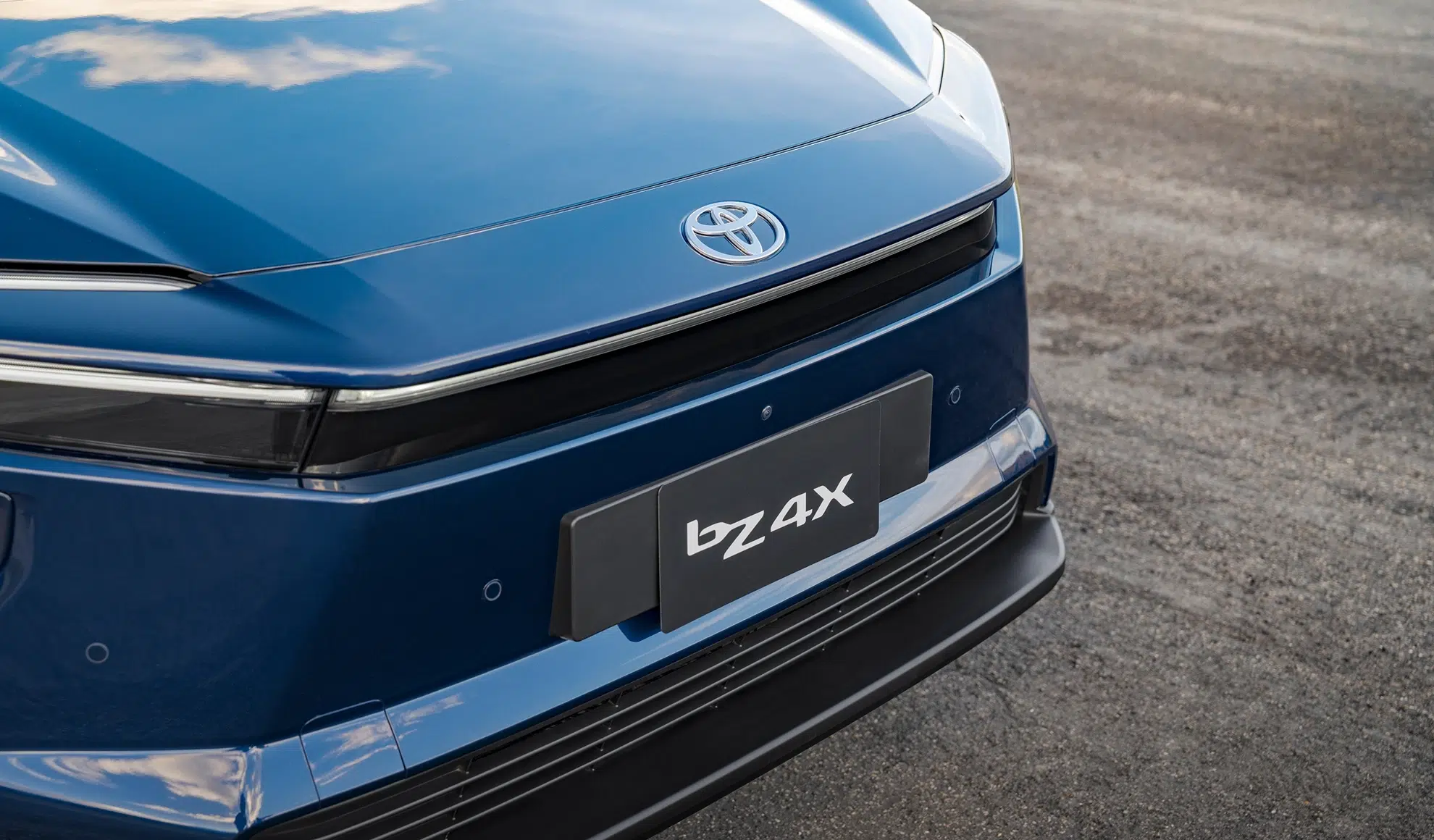 Blue Toyota car front end with emblem visible on the hood and a partial license plate reading 'bz 4x' on the bumper piece.