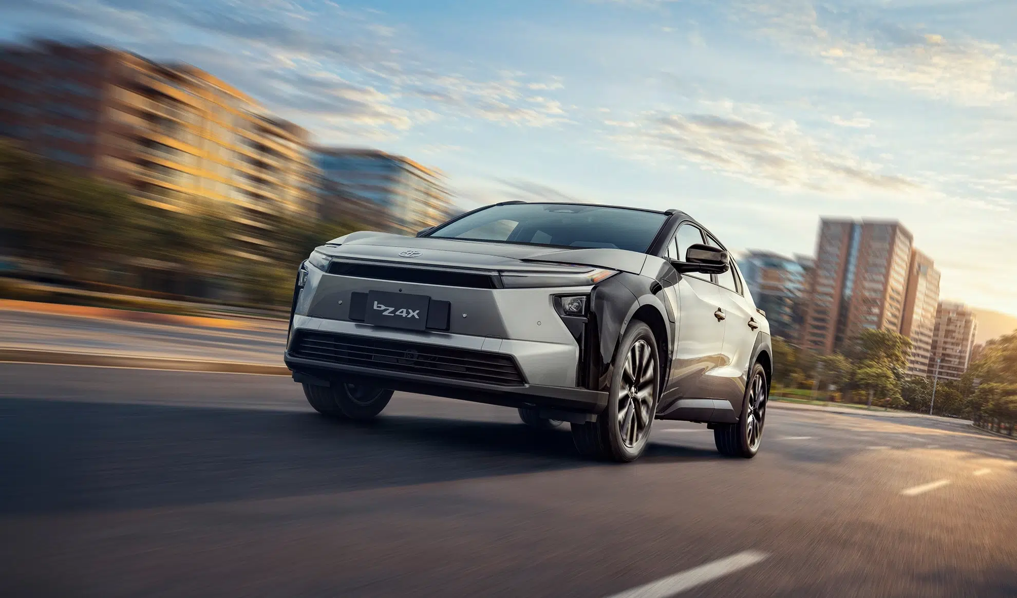 Silver Toyota bZ4X electric SUV driving on a city street with motion blur in the background.