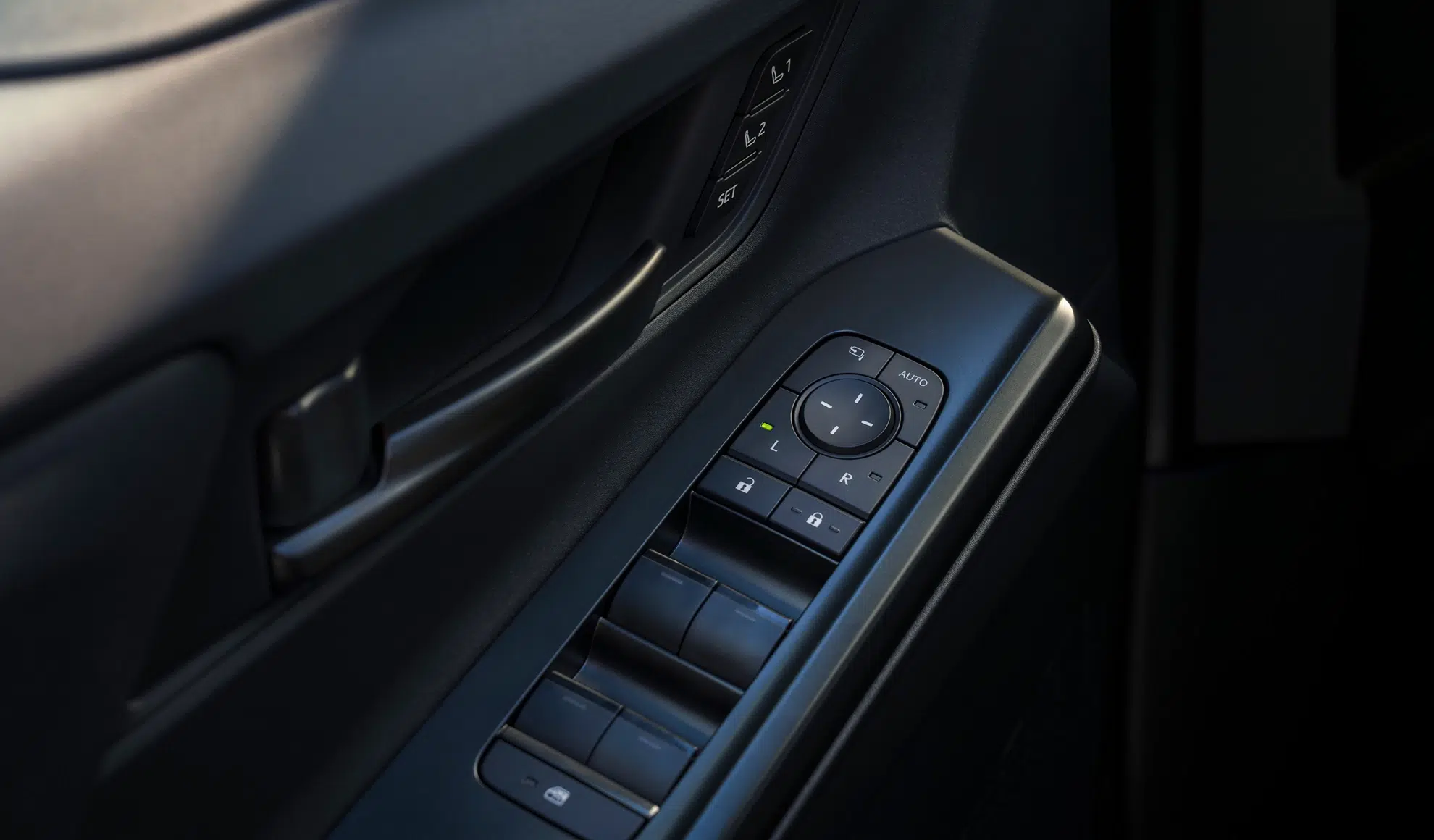 Close-up of a car door panel with window controls, a circular mirror-adjustment pad, and lock buttons on the armrest area.