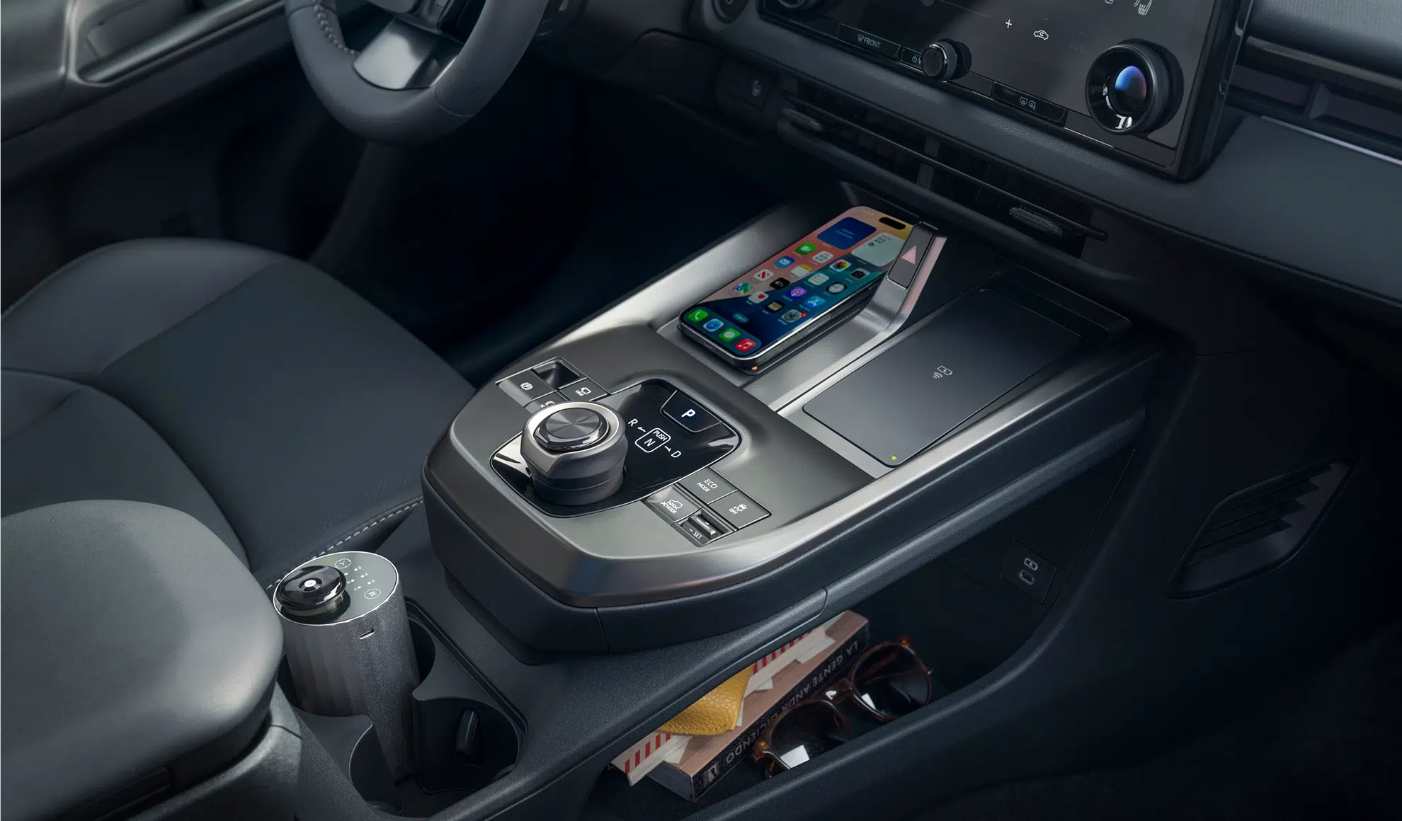 Center console with a smartphone on a wireless charging pad, adjacent gear shifter, and control panel in a modern car interior.