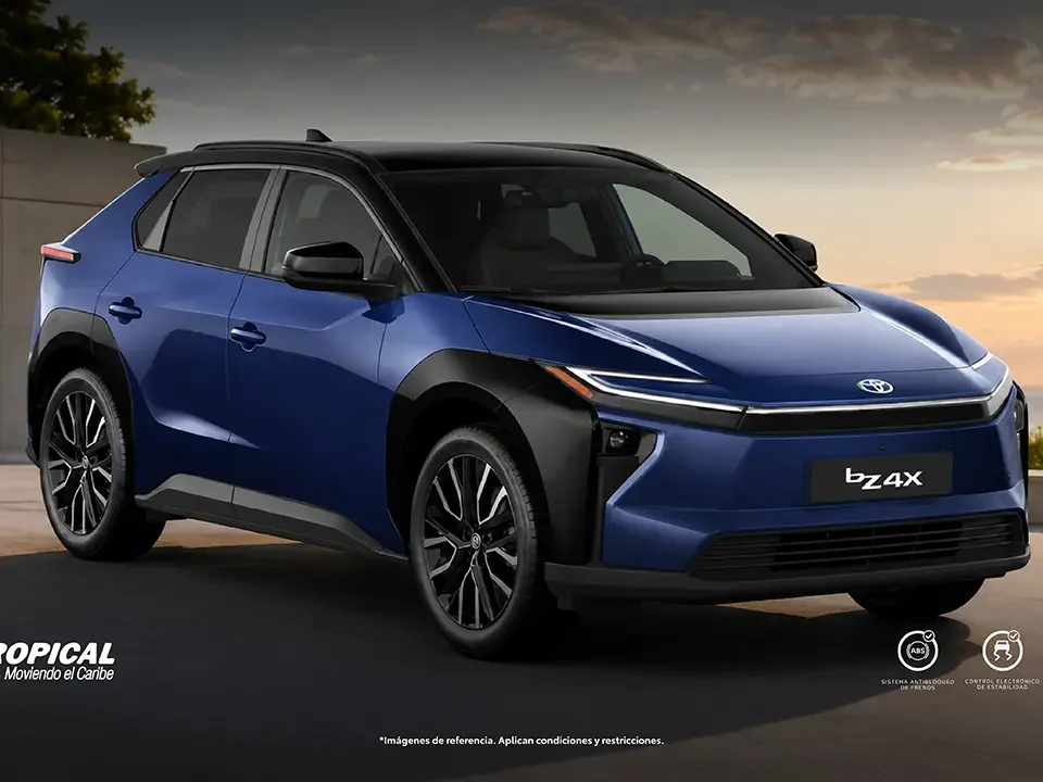 Blue Toyota bZ4X SUV parked outdoors at sunset, facing right, with Autotropical branding visible in the corner and Toyota logo overhead.