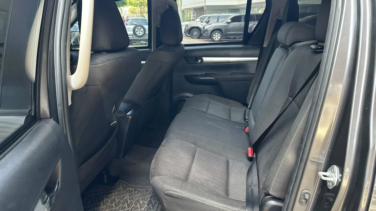 Rear interior of a dark gray SUV showing a three-person rear bench with headrests, seat belts, and patterned floor mats; passenger door open at the side.