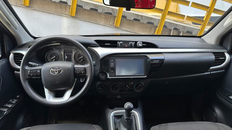 Driver's cockpit: steering wheel, dashboard with touchscreen, climate controls, and manual gear shift in view.