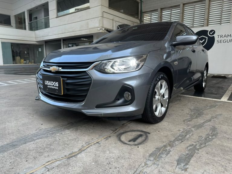 Front three-quarter view of a gray Chevrolet sedan with headlights on in a dealership lot, license plate visible