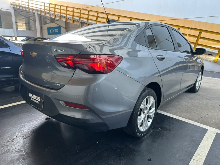 Rear three-quarter view of a gray Chevrolet sedan (LTZ) parked in a dealership lot, showing red taillights and glossy bodywork.