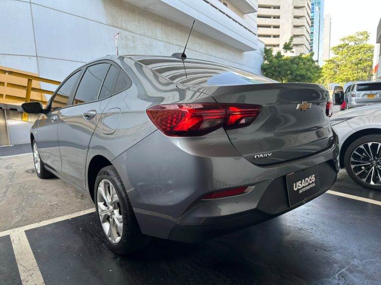 Rear three-quarter view of a gray Chevrolet Onix with red taillights in a parking lot at a dealership lot.