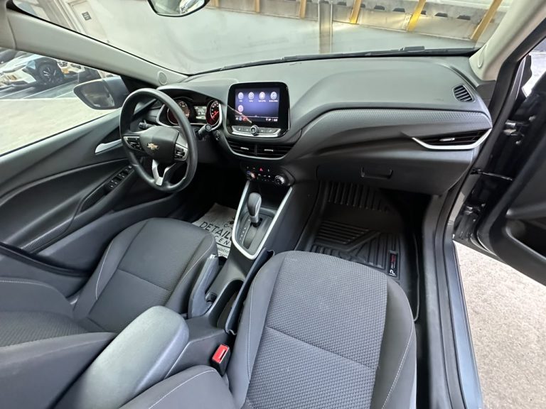 Driver's-side view of a modern car interior with a black fabric front seats, steering wheel, and center touchscreen display.