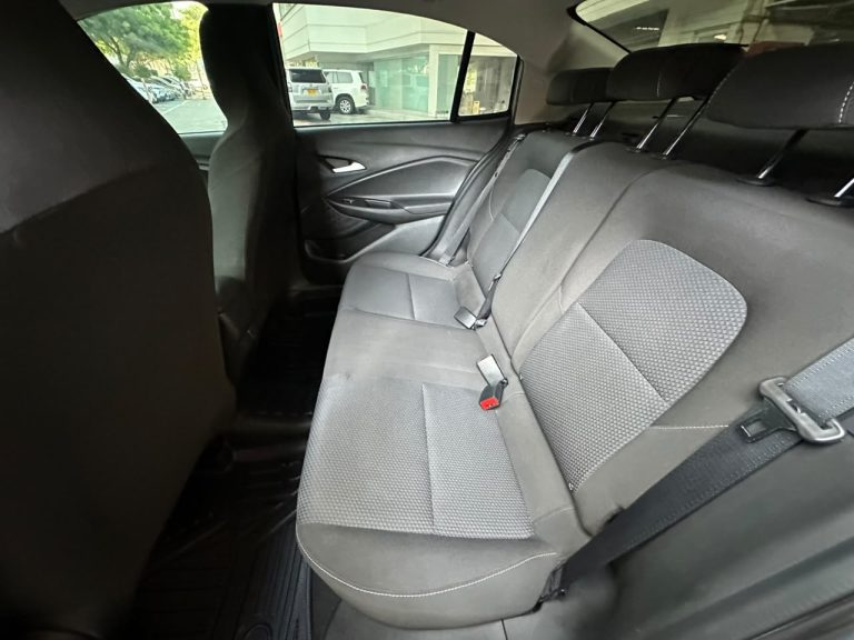 Back seat of a sedan with three gray fabric seats, headrests, and visible seat belts, viewed from the left rear door.