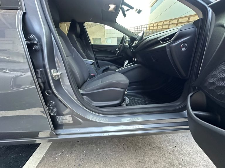 Open-driver-side door reveals the front seats and dashboard of a modern gray car, with a center console and floor mats visible inside.