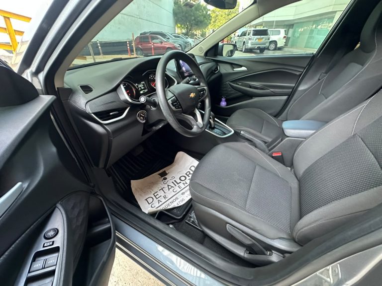Interior of a car cabin seen from the driver’s side, showing the steering wheel, center console, and front seats with a paper floor mat on the driver’s side.