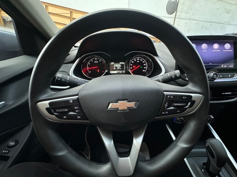 Close-up of a Chevrolet steering wheel with instrument cluster and infotainment screen behind it in a car interior.