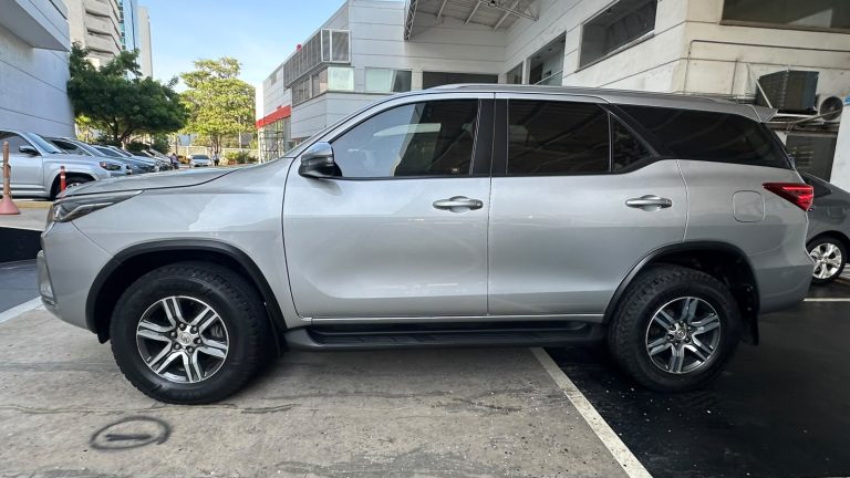 Side view of a silver mid-size SUV parked in a parking lot beside a modern building, with tinted windows and alloy wheels.