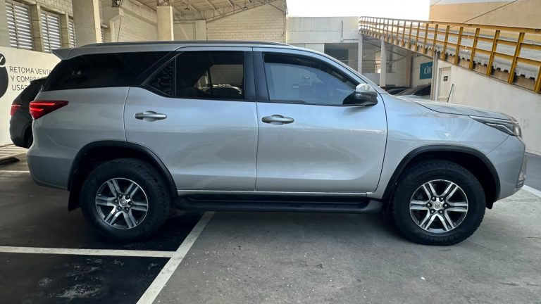 Side view of a silver SUV parked in a covered parking area, showing four doors and alloy wheels.