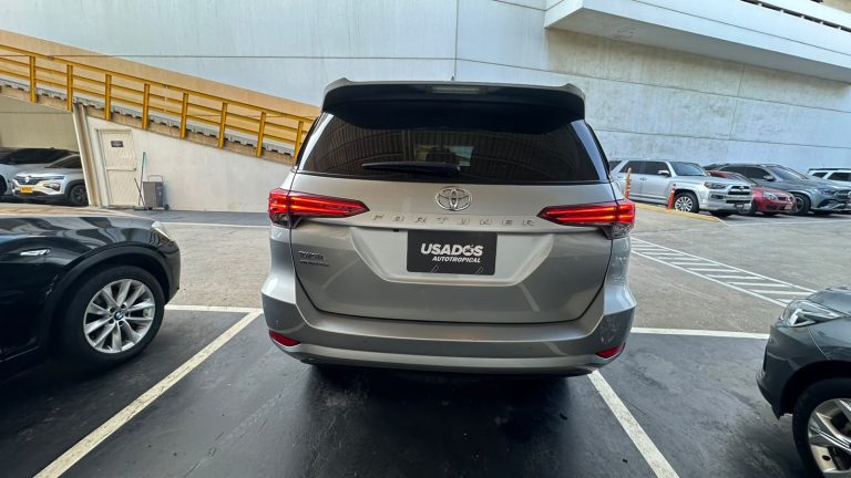 Rear view of a silver Toyota Fortuner SUV parked in a lot, with dealership plate visible on the bumper and other cars around it.