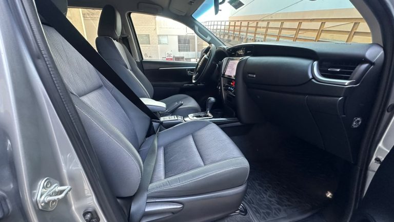 Interior of a modern car shown from the open front passenger door, featuring gray fabric seats, center console, and dashboard with touchscreen control.