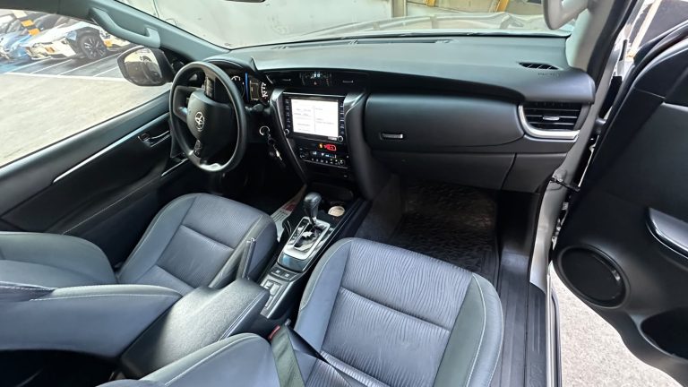 Interior of a modern car: left-hand drive, driver’s seat, steering wheel, center touchscreen, and gear shifter.