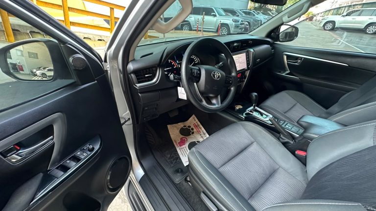 Open driver-side door view of a modern car interior showing steering wheel, dashboard, and center console with touchscreen display while parked.