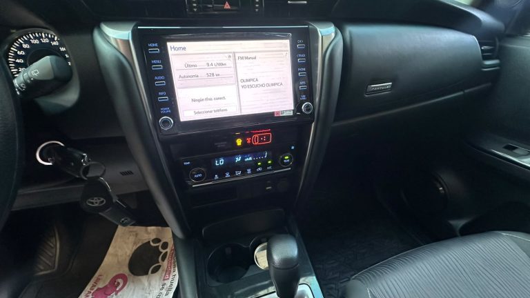 Car interior focused on the center console with a large touchscreen navigation/display and gear shift nearby, keys in the ignition.