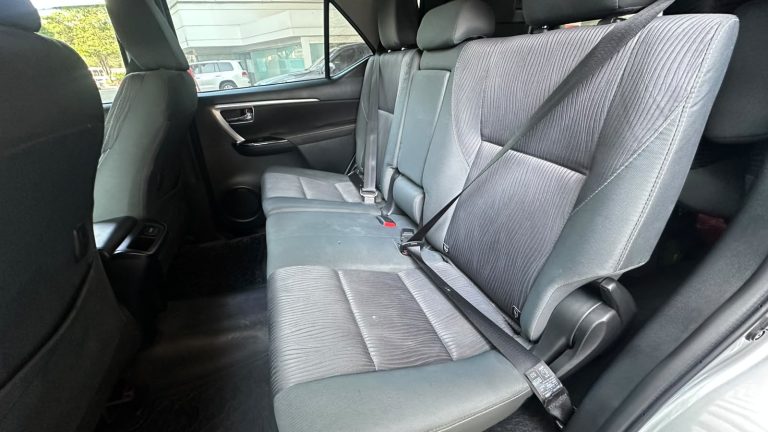 Rear seat of a car with three gray fabric seats and three seat belts, view from the passenger side side door area?
