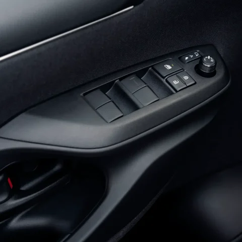 Close-up of a car's driver-side door panel showing power window switches, lock buttons, and a mirror adjustment knob on a dark interior surface.