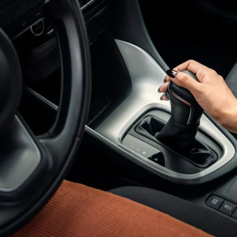 Close-up of a person's hand on the gear selector in a car, wearing a gold watch on the wrist.